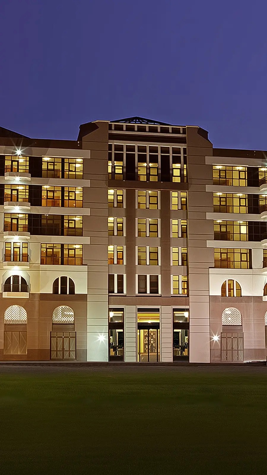 Lit mid-rise building facade at dusk with arched windows