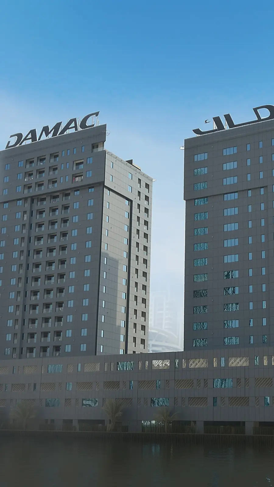 Two towers with DAMAC sign above a podium by the water