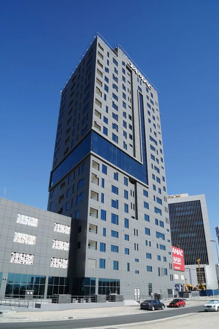 Full-height grey tower with blue glazing band and DAMAC crown