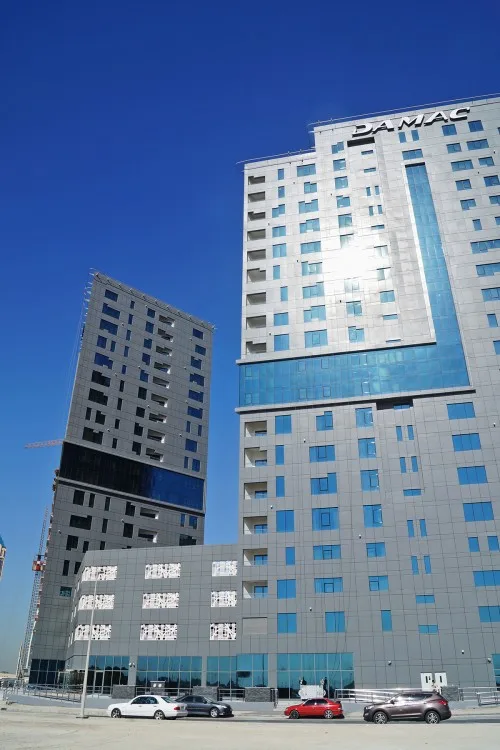 Capital Bay towers with podium, DAMAC signage, blue glass band