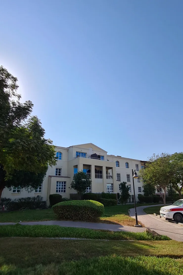 Cream apartment block with gabled centre, seen across gardens