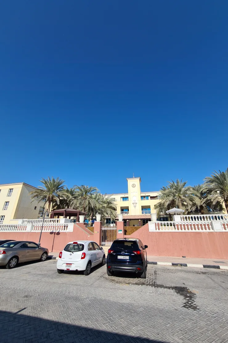Complex entrance with clock tower, palms and pink wall