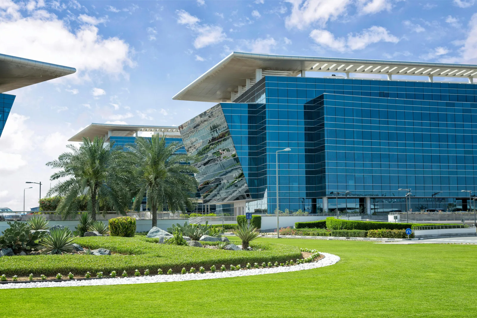 Blue glass office building with angled corner, landscaped lawn