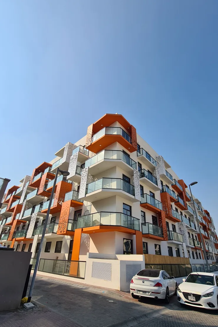 Corner of completed building with orange balconies and perforated panels